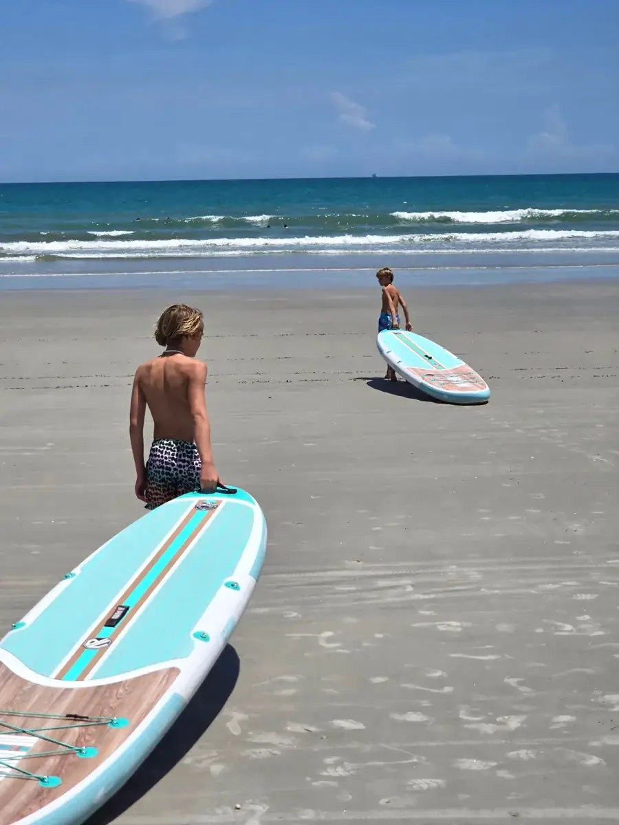 Kids dragging teal paddleboards on the beach